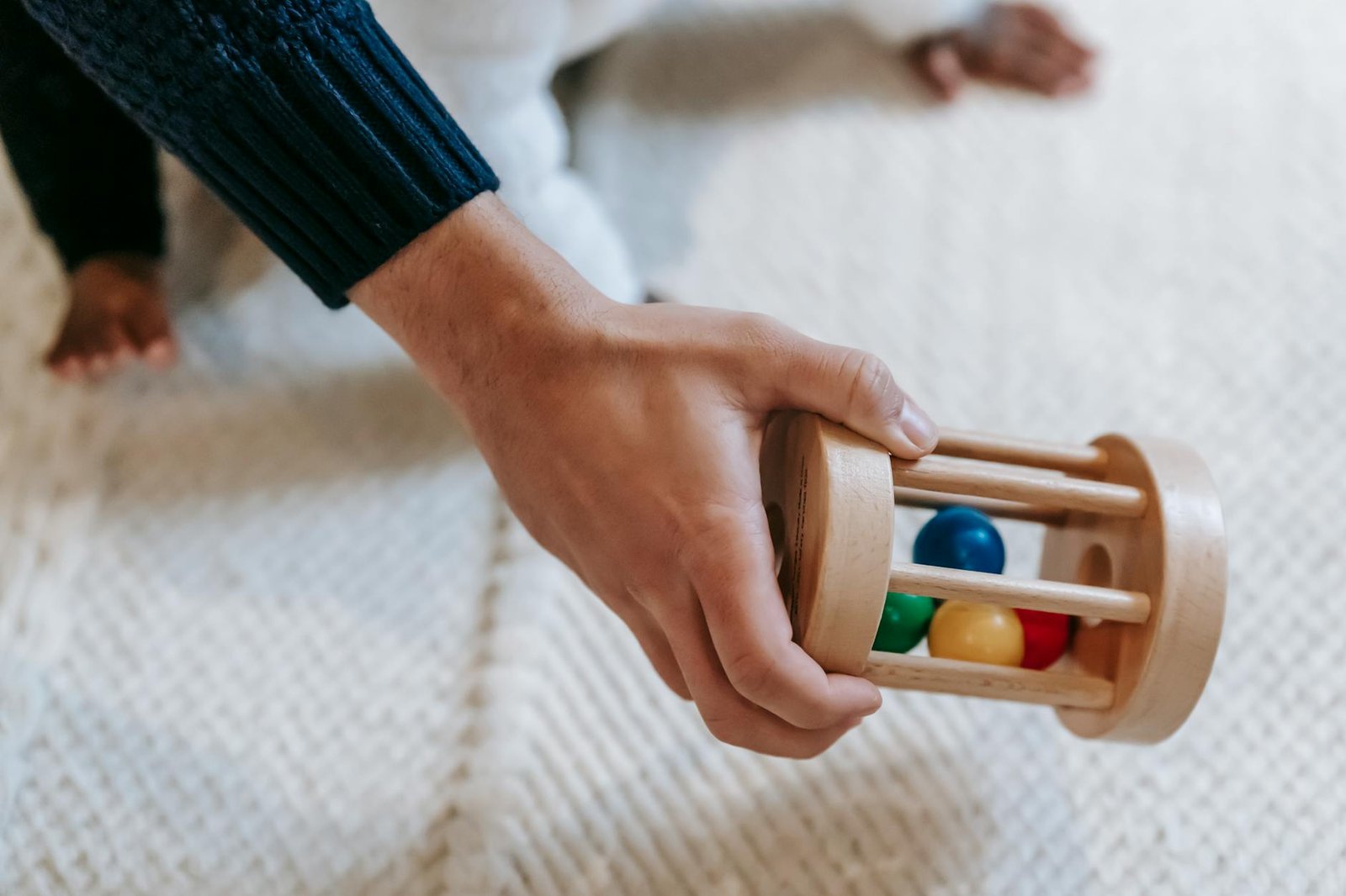 From above of crop anonymous male parent carrying colorful wooden rattle with small balls while spending time with little babyb